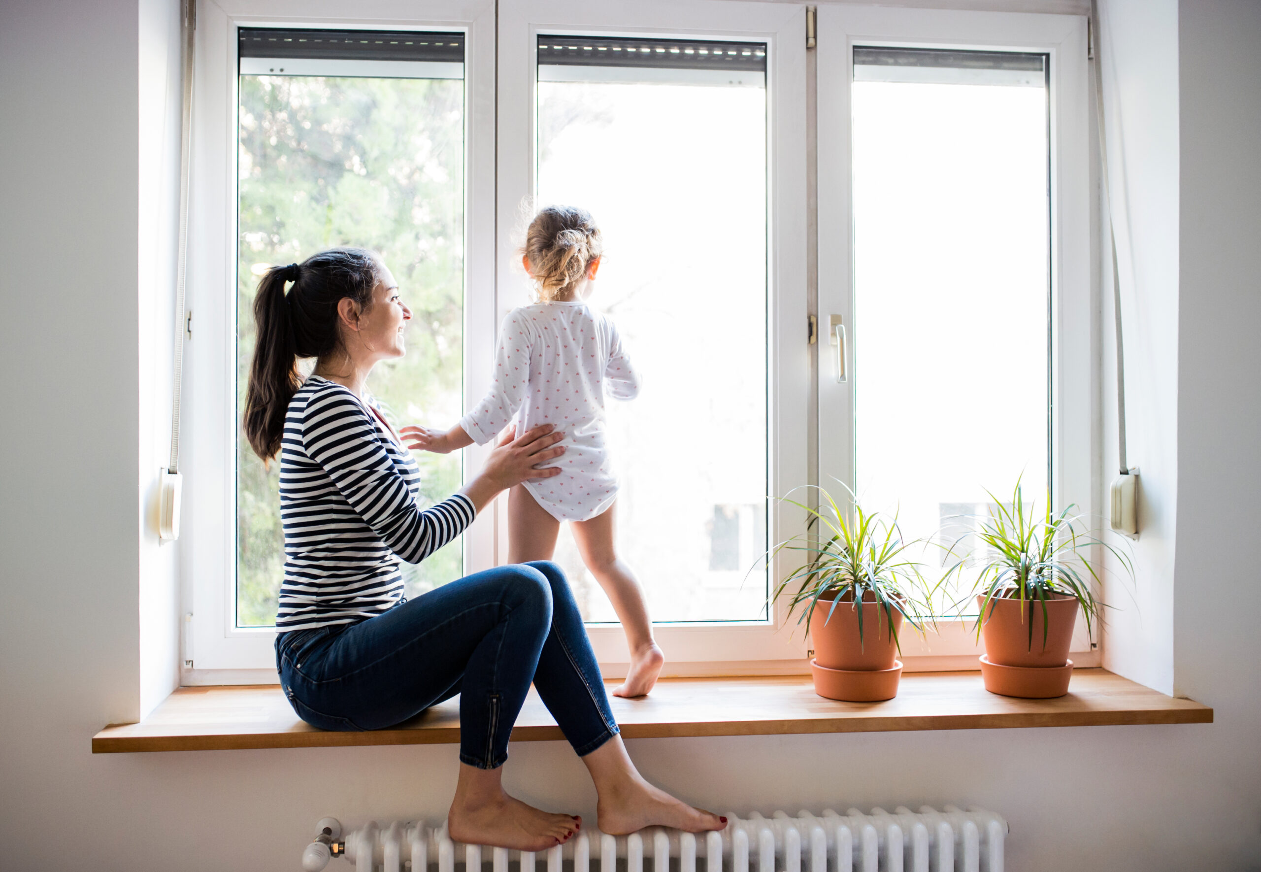 a young mother and her child standing next to double-paned windows as the sun shines through